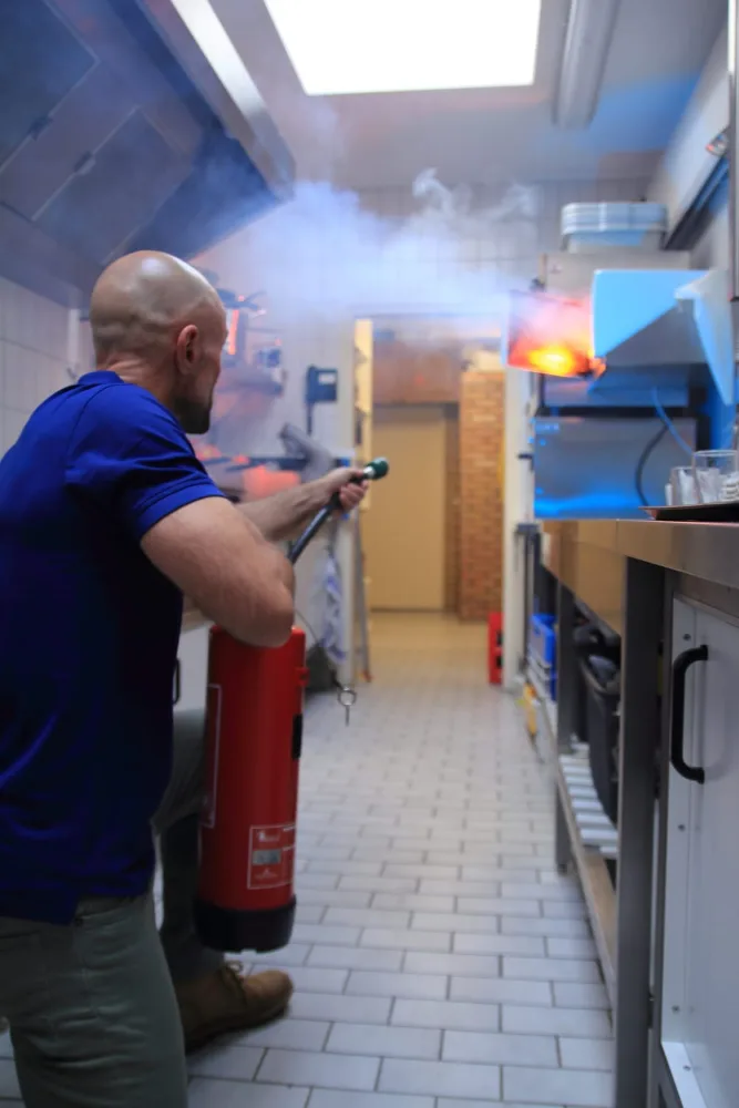 Deelnemer blust een keukenbrand onder begeleiding tijdens de BHV-training van Whyskills.